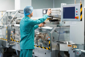 Pharmaceutical factory man worker in protective clothing operating production line in sterile environment